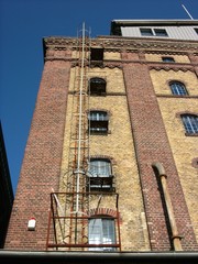 Rostige alte Feuerleiter an einem Getreidespeicher mit Backsteinfassade in Beige und Braun im...