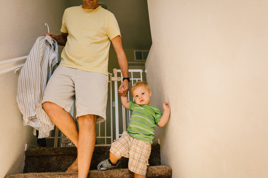 Father and young son walking downstairs, holding hands, father holding shirt on hanger