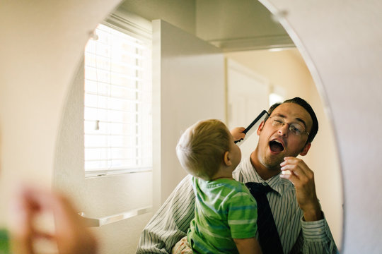Father holding young son, son trying to comb father's hair, reflected in mirror