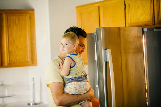 Father holding young son, looking in fridge