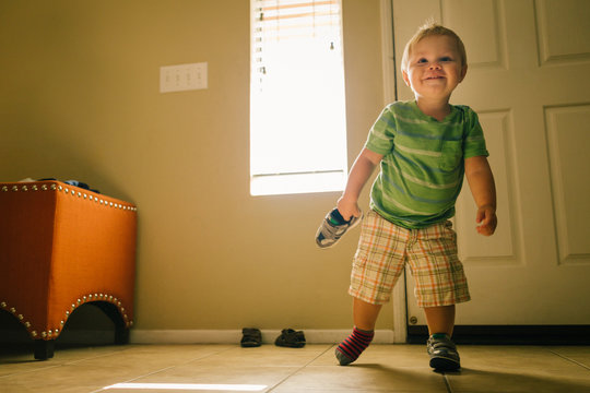 Young boy walking indoors, one shoe on foot and one in hand