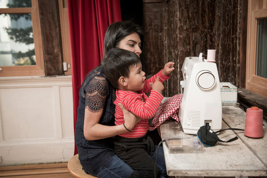 Male toddler sitting on mother's lap at sewing machine