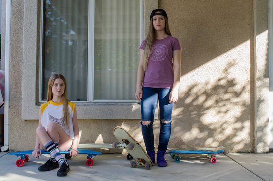 Portrait of two teenage skateboarder sisters on porch
