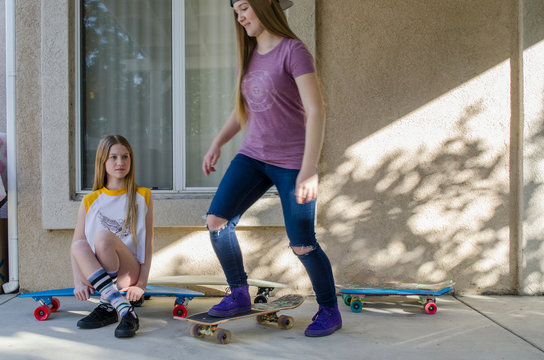 Two teenage skateboarder sisters practicing on porch