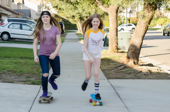 Two teenage skateboarder sisters skateboarding on sidewalk