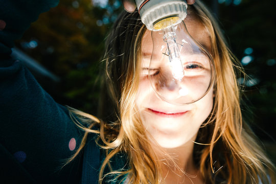 Portrait of girl holding illuminated lightbulb in garden at dusk