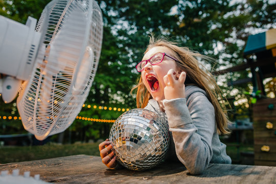 Girl screaming in front of windy electric fan at garden table