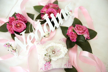Wedding arrangement of inscriptions, ribbons, flowers and wedding rings on a white bed
