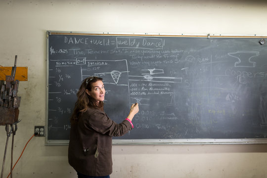Female metal work teacher writing on classroom blackboard