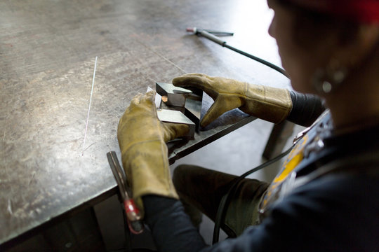 Over shoulder view of female metalsmith aligning metal at workshop bench