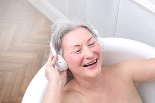 Senior woman smiling and listening to music in bath tub