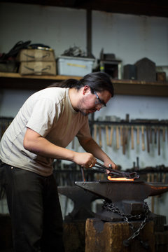 Male metalsmith shaping red hot metal on workshop anvil