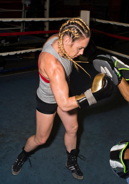 Female boxer punching trainer's boxing mitt in boxing ring