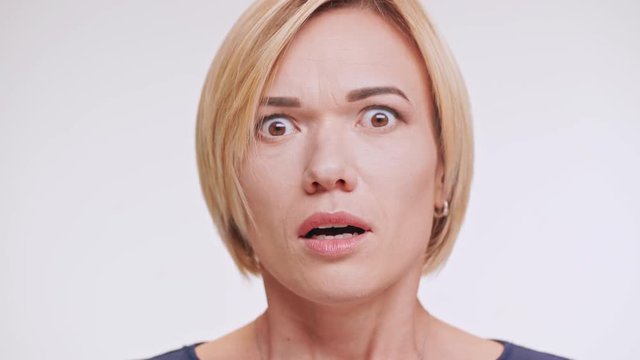 Close up footage of afraid Caucasian female with blonde hair standing on white background in shock