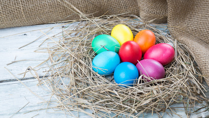 Colorful easter eggs in hay on wooden background