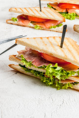 Club sandwiches with fresh lettuce, tomato, cucumber and salmon (trout). On crunchy toast. On the white stone concrete table, close view copy space vertical