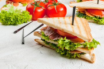 Club sandwiches with fresh lettuce, tomato, cucumber and salmon (trout). On crunchy toast. On the white stone concrete table, close view copy space, horizontal