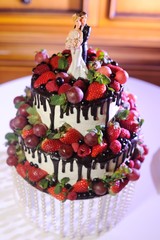 naked tiered cake with fruits and berries, and with figures of the bride and groom