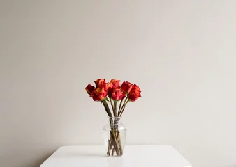 Photo sur Plexiglas Roses Red and orange roses in a glass vase on a white table against neutral wall