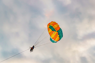 Skydivers on colorful Parachute at cloudy sky. Active lifestyle, extreme Hobbies. Couple parasailing on Pantai Tengah Beach, Langkawi island, Malaysia.