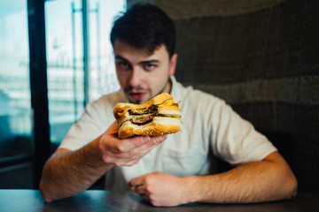 a young man sitting in a nice restaurant and offers a taste tasty burger
