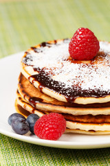 Pile of Pancakes with blueberries and raspberries, chocolate sauce and powder sugar