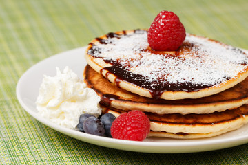 Pile of Pancakes with blueberries and raspberries, chocolate sauce and powder sugar