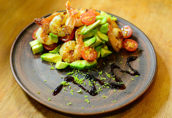 Fresh salad with fried shimps, raw avocado and tomatoes on clay dish