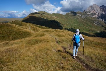 Fototapeta premium Wanderin unterwegs auf Bergwiese in traumhafter Bergkulisse in Gröden / Südtirol