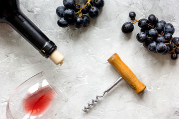 Bottle of red wine with corkscrew on white stone background