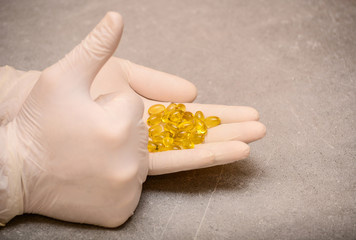 Hand wearing rubber glove holding gelatin softgels with vitamin D, health capsules, healthy diet concept