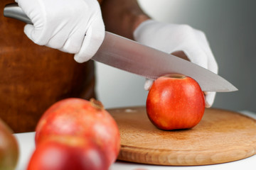 Close-up on hands in white gloves cutting an apple with the help of big sharp knife