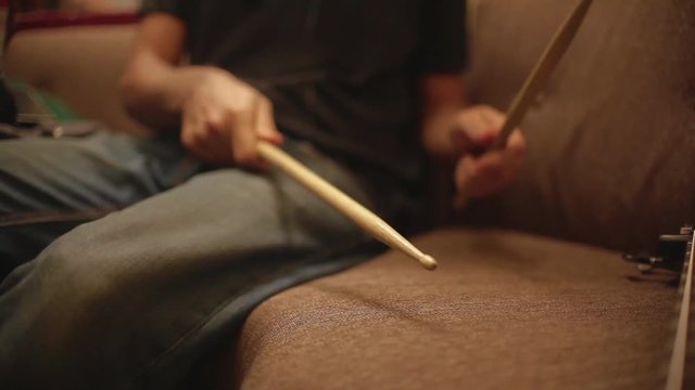 drummer practices on couch with drumsticks