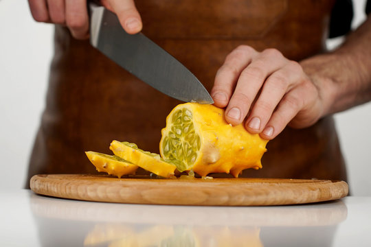 Man cutting tropical fruit kiwano into slices on a wooden cutting board on white background