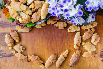 Homemade fresh cookies in bowl and violets flowers on wooden board with copy space, top view.