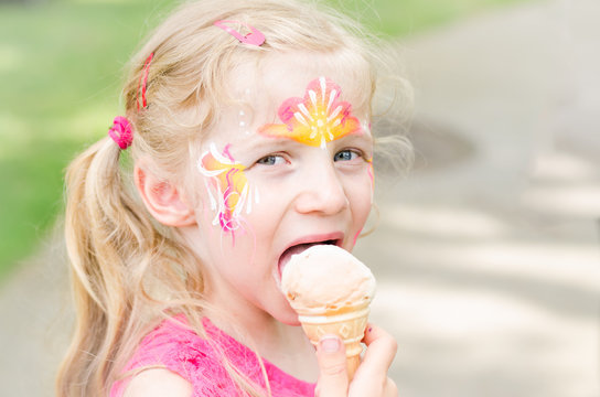 girl with colorful face-painting eating ice cream