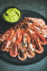 Roasted red shrimps with guacamole avocado sauce in slate stone black plate over grey concrete background, selective focus