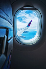 Plane window with blue sky and clouds