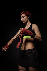 Woman is wrapping hands with red boxing wraps in dark room