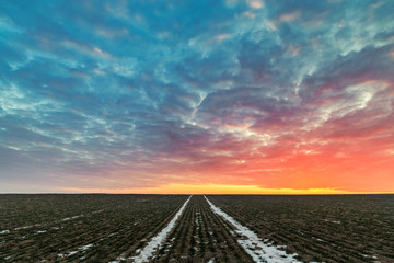 Fototapeta premium Sunrise Clouds over Vast Farming Field with Snow Trails in the Centre of Frame