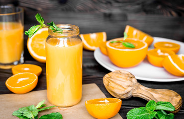 Cut oranges with juice in bottle and mint on kitchen background