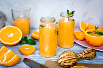 Cut oranges with juice in bottle and mint on kitchen background