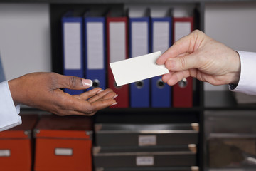 homme blanc caucassien tendant sa carte de visite dans un bureau à une femme noire 