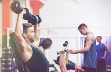 Athletic man training with dumbbells in gym