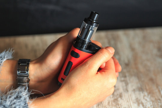 Red electronic cigarette in women's hands. Mechanical mod. ENDS.