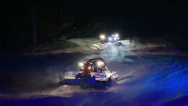 Snow groomers dancing in the snow at night