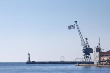 Fototapeta na wymiar Greek flag on a crane on Thessaloniki pier, Greece..Picture of a Greek flag on a crane seen in Thessaloniki, Greece, on the iconic pier of the old port