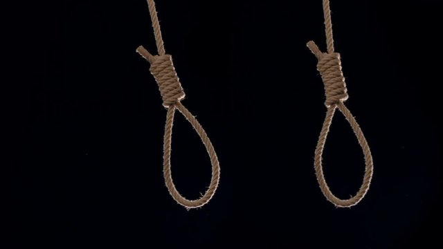 Two rope nooses swing adjacent to each other against black studio shot