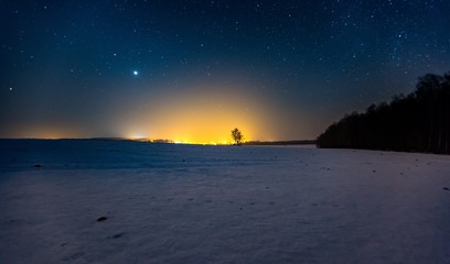 Milky way and starry sky over winter landscape and distant village