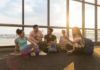 Young People Group Sitting On Floor In Airport Lounge Windows Waiting Departure Speaking Happy...